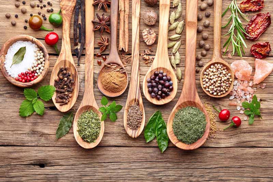 Wooden spoons full of spices and scattered herbs and seasonings 